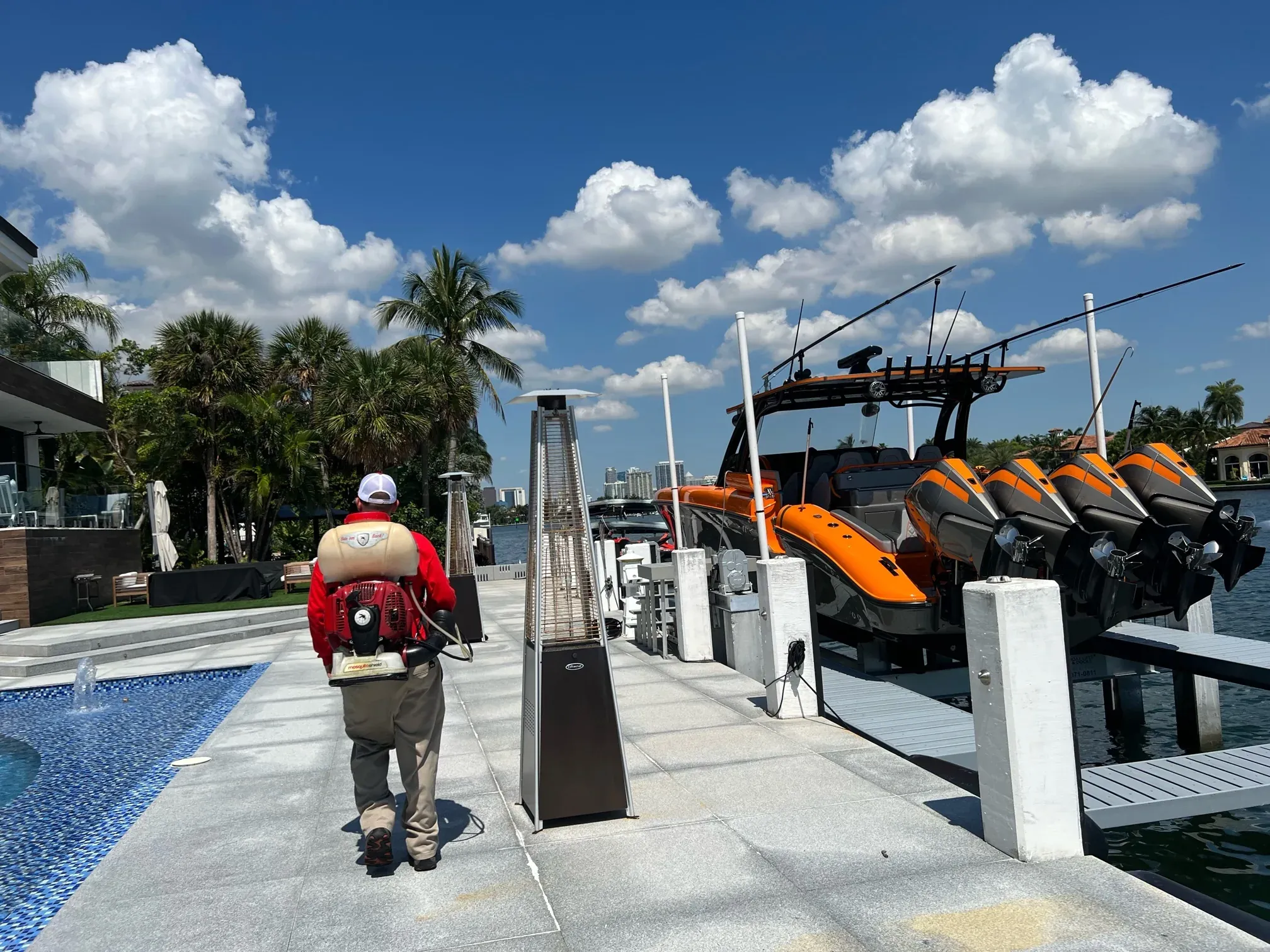 Mosquito Shield technician treating a luxury South Florida waterfront property with pool, boats, and palm trees