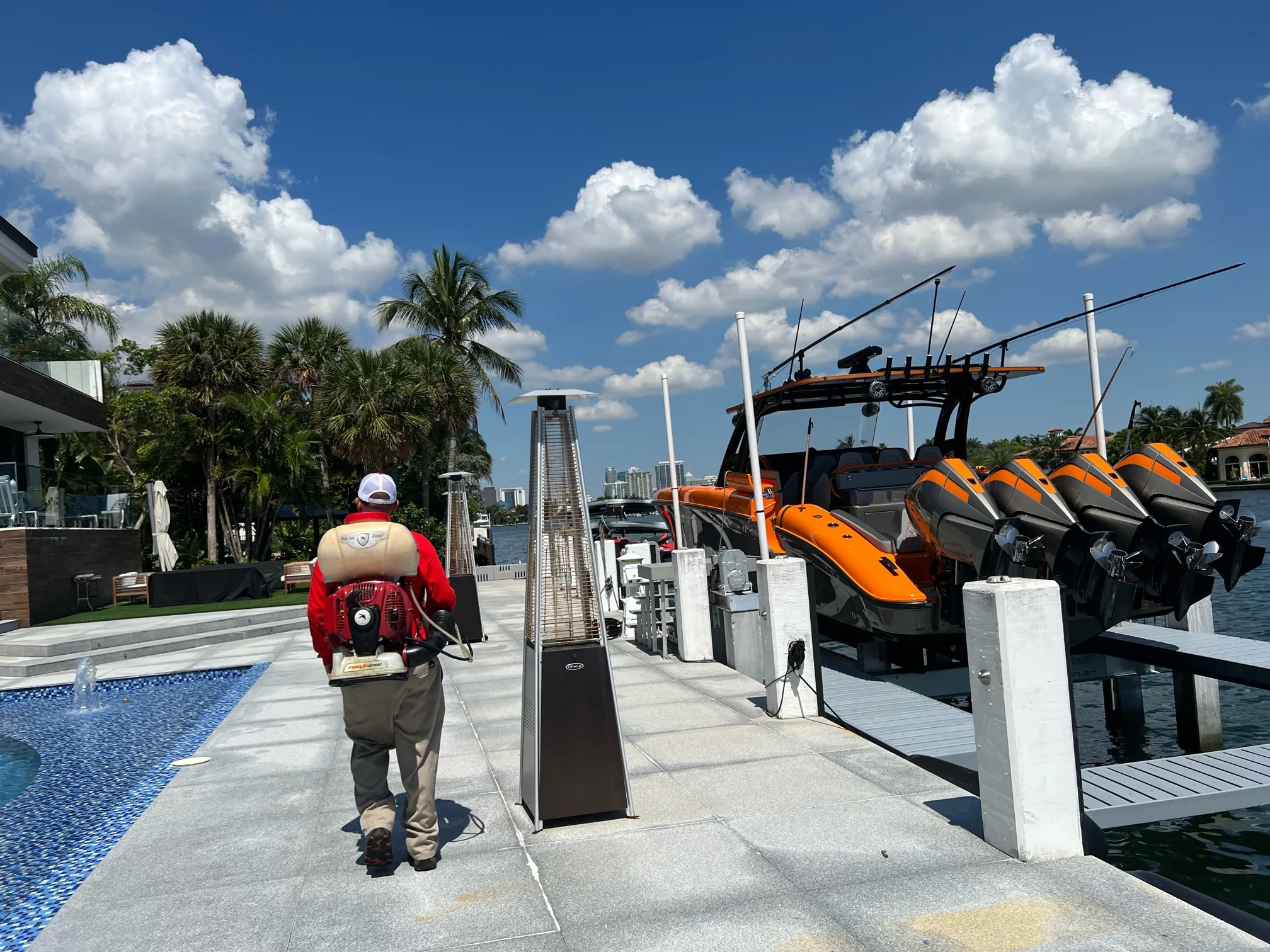 Mosquito Shield technician treating a luxury South Florida waterfront property with pool, boats, and palm trees